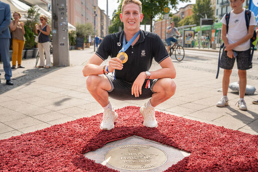 Bild vergrößern: Lukas Märtens mit Olympiamedaille vor seiner Bodenplatte